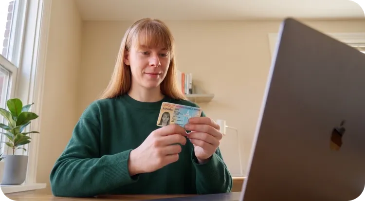 Hand holding an ID card next to a cell phone displaying the digital verification of the same document with a green confirmation icon
